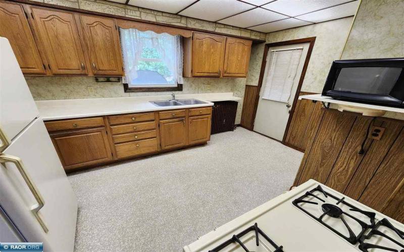 Kitchen with a refrigerator, gas range, and microwave, featuring a window above the sink.