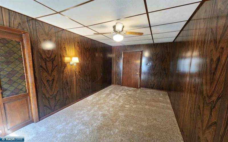 Carpeted main floor bedroom with a crop ceiling, ceiling fan, and wood paneling